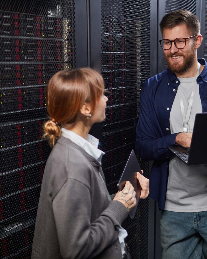 Image showing two IT professionals conversing in modern data center. Man holding laptop and woman holding tablet while standing in front of server racks